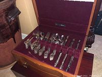 Open chest showing top tray with forks, spoons, knives and serving implements against burgundy velvet interior