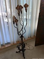 Full view of vintage metal standing lamp showing five curved arms with petal-shaped shades and bulbs, lamp standing near window curtains.