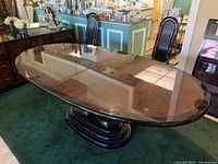 Oval lacquered dining table with Mertyl burl top and black lacquered oval base with metallic accents, shown from an angle.