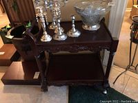 Front view of the wooden drink cart with some contents on top, showing carved legs and claw feet with wheels.