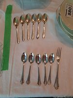 Five European silver spoons and one fork arranged in two rows on white fabric, spoon handles have decorative details with 800 silver markings. The fork has a matching handle design.