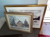 Two framed art pieces leaning against a wall, showing both paintings and their frames.