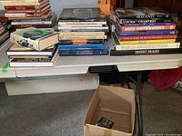 Wide view of 2 bins of hardcover books stacked on a folding table showing various titles related to travel, art, and history.