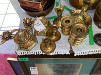 Photo showing a collection of brass candle holders in different designs placed on a table with a white cloth.