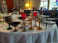 Wide shot of assorted metal and silver plate candle holders and decorative items on table.