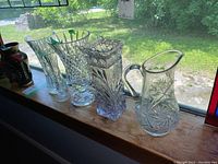 Photo of all five items on window ledge showing four crystal vases and one crystal pitcher in natural light.