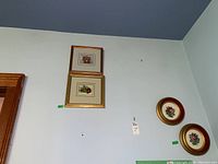 Four framed flower artworks hung on wall, two small circular needlepoint framed pieces and two larger rectangular framed floral pieces.