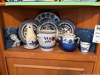 Blue and white ceramic dishes, vases, pitcher, teapot, and decorative tiles on a wooden shelf.