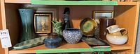 Overview image showing multiple pottery items and two small framed paintings arranged on a wooden shelf.