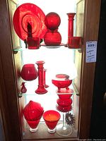 Full shelf of ruby red glass items including candle holders, plates, bowls