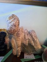 Front side view of the polished stone sculpture showing rounded head and carved body details on a wooden surface against a white wall.