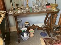 Console table with decorative curved legs, stretched wood support, medium-tone wood finish, displaying various glass and ceramic items (contents not included).
