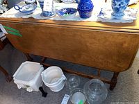 Full view of wooden table with drop leaves down, showing warm wood grain and turned legs, various decorative items on top are excluded from sale.