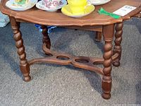 Photo of ornate wooden side table showing scalloped edge top and turned legs with decorative stretcher base.