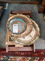 Stack of three round wooden plates with scalloped edges showing painted floral and geometric designs placed on a wooden tray with recessed panel base, exhibiting wear and paint chips.