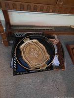 Four stacked trays of different styles and materials, including the ornate floral rectangular tray on top, black round metal tray beneath, and rustic wooden trays at bottom.