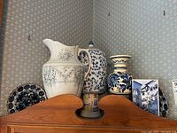 3 vases and 2 decorative plates arranged on wood shelf with Portugal wall hanging visible