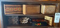 Top view of two shelves containing several small wooden boxes with intricate designs and wood bird carving.