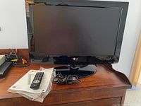 Photo of the LG 26-inch flat screen TV on wooden desk, showing TV screen, base, HDMI cord and cables underneath.