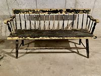 Front view of antique wood deacon's bench showing peeling black and cream paint on slatted back, seat and arms.