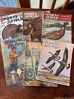Six vintage hunting and fishing magazines laid out on a wooden table