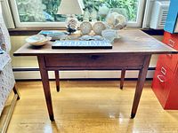 Front view of antique wooden tavern table showing entire table with various items on top with visible wear and wood grain.
