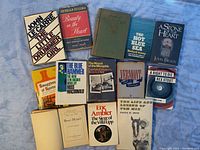 Photo showing 12 vintage books laid out on blue background, titles clearly visible including The Little Drummer Girl by John Le Carre and The Hot Blue Sea by Richard McMillan.