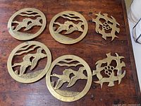 Overview of all six brass trivets on wooden surface, showing four round duck trivets and two smaller uniquely shaped bird trivets.