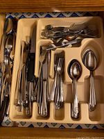 Full view of beige plastic cutlery tray filled with mixed metal knives, forks, spoons of varying styles and sizes.