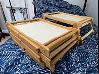 Set of 4 wooden folding lap trays stacked and one unfolded on a bed with blue patterned bedding.