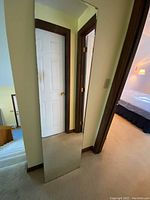 Full length mirror propped against a wall next to a door, showing its height and beveled edges.