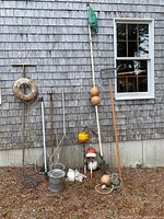 Wide view of the lot lined up against weathered wooden shingles, showing life saver ring, buoys on poles, nets, rakes, buckets, ropes, and a wooden oar.