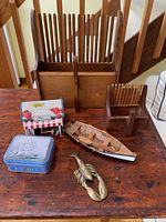 Photo showing the whole lot arranged on a wooden table including the cranberry rakes, lobster music box, wooden rowboat model, sailboat tin and brass lobster door knocker.