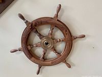 Front view of the wooden ship's wheel wall decor showing natural wood grain and brass-colored center hub.