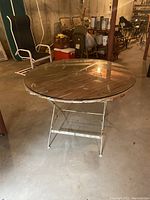 View of the vintage round wood slat table with glass top in a basement setting showing the full table with metal legs and visible rust.