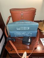Blue box labeled Stellarscope with electrical adapter placed on top of brown carrying case