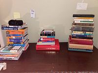 Overview of three stacks of books on a table: travel books on left, dictionaries and thesaurus center, vintage fiction stacked right