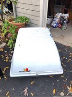 Top and side views of the white Sears X-Car cargo carrier box resting on asphalt near plants and outdoor items.