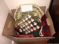 Box showing ceramic platters, napkins, cookbooks and candles together.