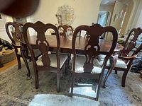 Dining table with leaf and 8 matching carved wood chairs arranged around it, showing front and rear views of chairs and table surface.