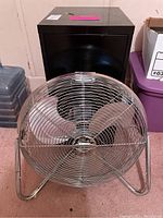 Black metal file cabinet with a Lakewood metal fan in front on a carpeted floor