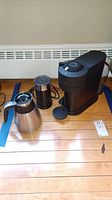 Nespresso coffee brewer, corded grinder, and coffee pot arranged on wooden floor.