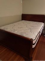 Full view of queen size sleigh bed frame including headboard, footboard, and mattress on hardwood floor.