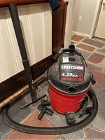 Craftsman red and black wet/dry shop vacuum with hose, extension tubes attached and on floor beside it.