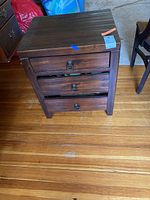 Front view of dark wood side table showing three drawers with metal ring pulls, and visible scratches on wood.
