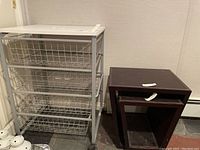 Rolling metal storage drawer cart with wire mesh drawers and white top next to two nesting tables.