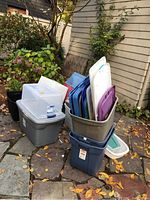 Photo of various plastic storage bins stacked and grouped outdoors, showing bins and lids in multiple colors and sizes.