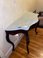 Full view of vintage hall table showing white marble top and dark carved wooden base with curved legs
