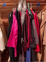 Clothes hanging on wooden rack showing dresses and blouses in various colors and styles.
