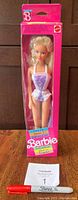 Front view photo of Barbie "Dress Me" doll in original unopened pink box with clear window, showing doll dressed in purple and white swimsuit.
